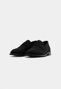 Svarta loafers gjorda av mjukt tyg, med en platt, rund tå, minimala sömmar och en kontrasterande gummisula.