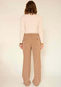 Pantalon large beige avec une texture lisse, deux poches arrière et une coupe ajustée, associé à un haut crème à manches longues ajusté.