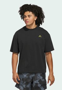 Zwarte korte mouwen t-shirt van katoen, met een klein geel driehoekig logo op de linkerborst. De pasvorm is ontspannen en boxy.