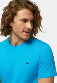 T-shirt in cotone blu con scollo rotondo e maniche corte, decorata con un piccolo logo di un bassotto nero sull'area sinistra del petto.