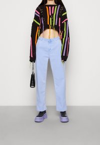 Pull cropped noir avec des rayures colorées, jean droit bleu clair, et chaussures à plateforme violettes. Comprend un petit sac à main noir.