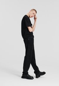 Camiseta negra de manga corta combinada con vaqueros negros holgados. El material parece suave; los vaqueros presentan un cosido sutil y calzado negro resistente.