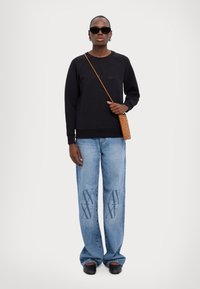 Felpa nera con polsini a coste, vestibilità rilassata. Jeans a gamba larga blu chiaro con design ricamato "AX". Occhiali da sole neri e borsa intrecciata marrone.