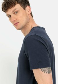 Marineblauwe katoenen t-shirt met korte mouwen, ronde halslijn en subtiele logo op de linker mouw. Gladde textuur, klassiek aansluitend ontwerp.