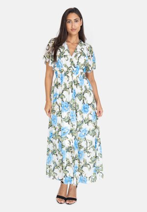 Blomstret maxikjole i hvid med blå blomster og grønne blade. Korte flæseærmer, strammet talje og flagrende skørt. Sorte sandaler med åben tå.