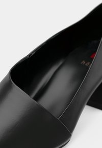 Chaussure en cuir noir à petit talon bloc, avec un bout arrondi et une finition lisse et polie.