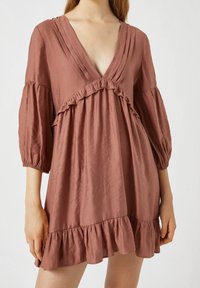 Kurzes, blush-pink Kleid mit tiefem V-Ausschnitt, Puffärmel und Rüschendetails am Oberteil und Saum. Hergestellt aus leichtem Stoff.