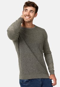 Grå tekstureret sweater med rund hals, der har en ribbet øverste sektion og lange ærmer. Bæres med blå jeans, der viser en afslappet pasform.