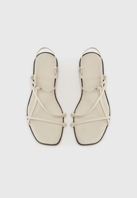 Beige litte sandals med en strappy design, der har tynde stropper og firkantet tå. Sorte såler og minimalistiske hardware-detaljer.
