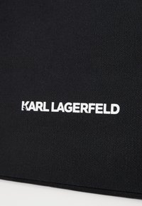 Black textured fabric with white "KARL LAGERFELD" branding. The design features a simple, modern aesthetic suitable for bags or accessories.