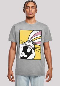 Pelēka T-krekls ar lielu melno, balto un rozā karikatūru truša grafiku uz dzeltena kvadrāta fona. Īsās piedurknes, arapa dizains.