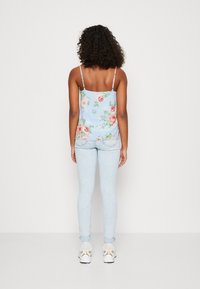 Modrý květinový top na tenkých ramínkách se vzorem růžových růží a zelených listů; doplněný o světle modré úzké džíny a bílé tenisky.