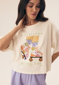 Kremowy crop top z krótkimi rękawami, z kolorową grafiką rolki i napisem. Wykonany z miękkiej bawełny, luźny krój.