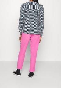 Blouse à manches longues, avec un motif géométrique noir et blanc, associée à un pantalon rose vif et des baskets noires.