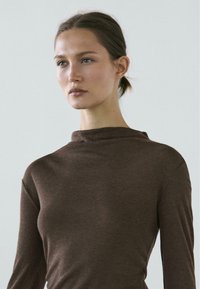 Braunes Langarmoberteil mit hohem Kragen, hergestellt aus weichem, strukturiertem Material, mit minimalistischem Stil und figurbetonter Silhouette.