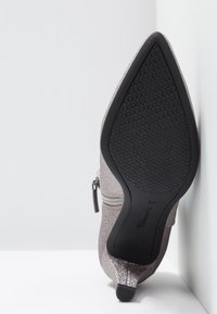 Bottine à paillettes à bout pointu posée sur le côté, montrant la semelle noire texturée et un petit talon avec une fermeture éclair latérale. Taille 37.