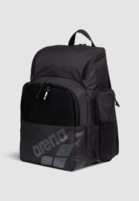 Zaino nero realizzato in nylon resistente, dotato di scomparti con cerniera, dettagli in rete e un grande logo sulla parte frontale. Design strutturato.
