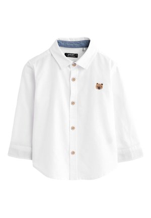Chemise pour tout-petit à manches longues blanche avec boutons en bois, doublure intérieure du col bleue et petit visage d'ours brodé sur le côté gauche de la poitrine.