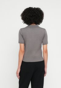 Rövid ujjú, világosszürke kötött póló, bordázott gallérral és szegéllyel. Simaclú, testhezálló szabású, letisztult részletekkel.