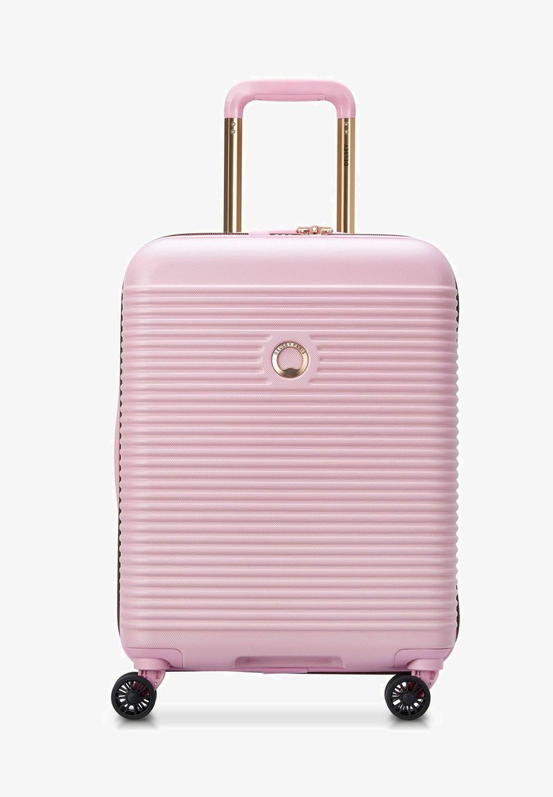 Valise rigide rose avec un design strié, poignées télescopiques dorées, roues noires et un détail en forme de logo circulaire sur le devant.