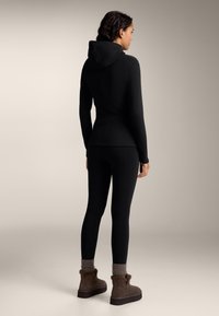 Zwarte getailleerde hoodie met een capuchon, gecombineerd met zwarte leggings. Bruine enkellaarsjes met bontaccenten. Gladde, elastische stof met een gestroomlijnd ontwerp.