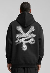 Sudadera negra con capucha que presenta un estampado gráfico de manos de esqueleto y calaveras en blanco en la parte posterior. Tejido suave, corte relajado, capucha con cordón.