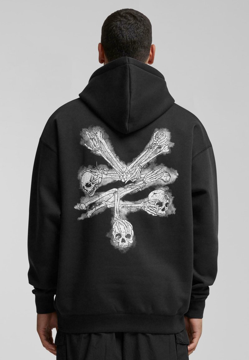 Sudadera negra con capucha que presenta un estampado gráfico de manos de esqueleto y calaveras en blanco en la parte posterior. Tejido suave, corte relajado, capucha con cordón.