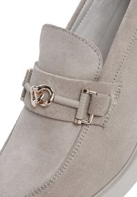 Mocassino in suede beige con un tocco metallico e un design a doppio anello, una fascia texturizzata e una suola bianca liscia.