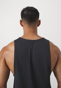 Fekete ujjatlan póló kerek nyakkal, texturált anyagból, hátul díszítő részlettel. Feszes fazon, széles karöltőkkel.