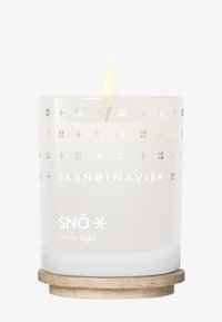Bougie blanche brûlante dans un porte-bougie en verre avec des symboles scandinaves et le texte "SNÖ Lumière d'hiver" sur une base en bois.