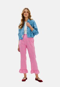 Světle modrá denimová bunda s květinovými vzory, bílý top, kalhoty v růžovém károvaném vzoru s volánovými nohavicemi a červené ploché boty.