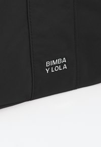 Borsa in tessuto nero con un logo argentato lucido che reca la scritta "BIMBA Y LOLA" su un lato, con una texture liscia e un design minimalista.