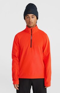 Oranje fleece pullover met hoge kraag, kwart-rits stijl, voorzien van een zwarte rits en logo, gecombineerd met een marineblauwe beanie.