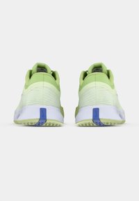 Ein Paar hellgrüne und weiße Sportschuhe mit blauen Fersenlaschen, von hinten auf einem schlichten weißen Hintergrund betrachtet.