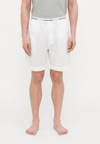 Baltā kokvilnas apakšbikses ar gludu tekstūru, aprīkotas ar platām elastīgām jostas vietām ar "Calvin Klein" logo. Īss garums un vienkāršs dizains.