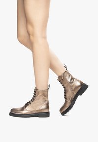 Bottes de cheville en bronze métallique avec une finition texturée, avant à lacets, et une languette, dotées d'une semelle en caoutchouc noir et d'un surpiquage contrasté.