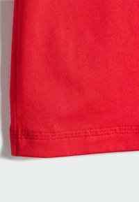 Crvena pamučna tkanina glatke teksture. Rub je uredno završen šavom. Nema vidljivih uzoraka ili ukrasa.