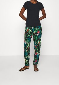 Sort ribbet tanktop med korte ærmer, parret med bukser med tropisk mønster, der har grønne blade og røde blomster; båret med sorte flade sandaler.