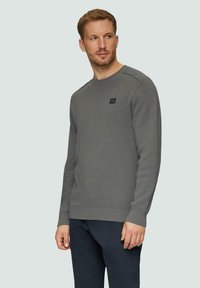 Pull gris à col rond en maille douce, avec une étiquette logo noire sur la poitrine et des poignets et un ourlet côtelés.