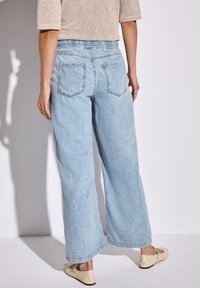 Helle blaue weite Jeans mit einem elastischen Bund, fünf Taschen und einer verblassten Textur, kombiniert mit neutralen Ballerinas.