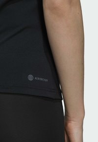 Fekete AEROREADY sportpóló, sima textúrával, rövid ujjakkal, logóval a szegély közelében, fekete, testhez simuló leggingssel párosítva.
