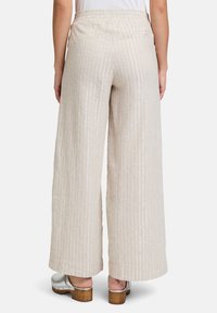 Szerokie, beżowe spodenki lniane w białe pionowe paski, z elastycznym pasem i luźnym krojem. W zestawie z srebrnymi sandałami na obcasie.