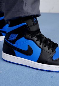 Črne in modre visoke superge s usnjenim in sintetičnim zgornjim delom, z belo srednjo podplatom, črnimi vezalkami in logotipom Air Jordan na strani.