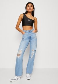 Top corto nero con una spallina e logo Puma, abbinato a jeans strappati a vita alta di un blu chiaro e scarpe da ginnastica bianche. Design a gamba dritta.