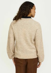 Bež pleteni pulover z ohlapnim krojem, okroglo ovratnikom in spuščenimi rameni. Mehak tekstura z rahlim mešanim vzorcem.