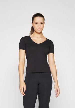 Svart t-skjorte med kort erme og v-hals laget av myk, glatt stoff, tettsittende design. Brukt sammen med svarte leggings, vist mot en lys bakgrunn.