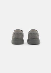 Gray suede sneakers with a rounded shape, flat rubber sole, and gold text branding on the heel. Minimalist design with clean lines.
