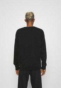 Svart sweatshirt med rund halsringning och långa ärmar. Har en rektangulär patch på baksidan samt ribbad mudd och nederkant.