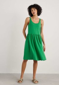Groene katoenen jurk met een getailleerde bovenzijde, uitlopende rok en ronde halslijn. Heeft brede bandjes en een geraffineerde taille.