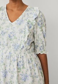 Robe fleurie en tissu léger avec des motifs de fleurs bleues et vertes, décolleté en V, manches volantées et taille élastique.